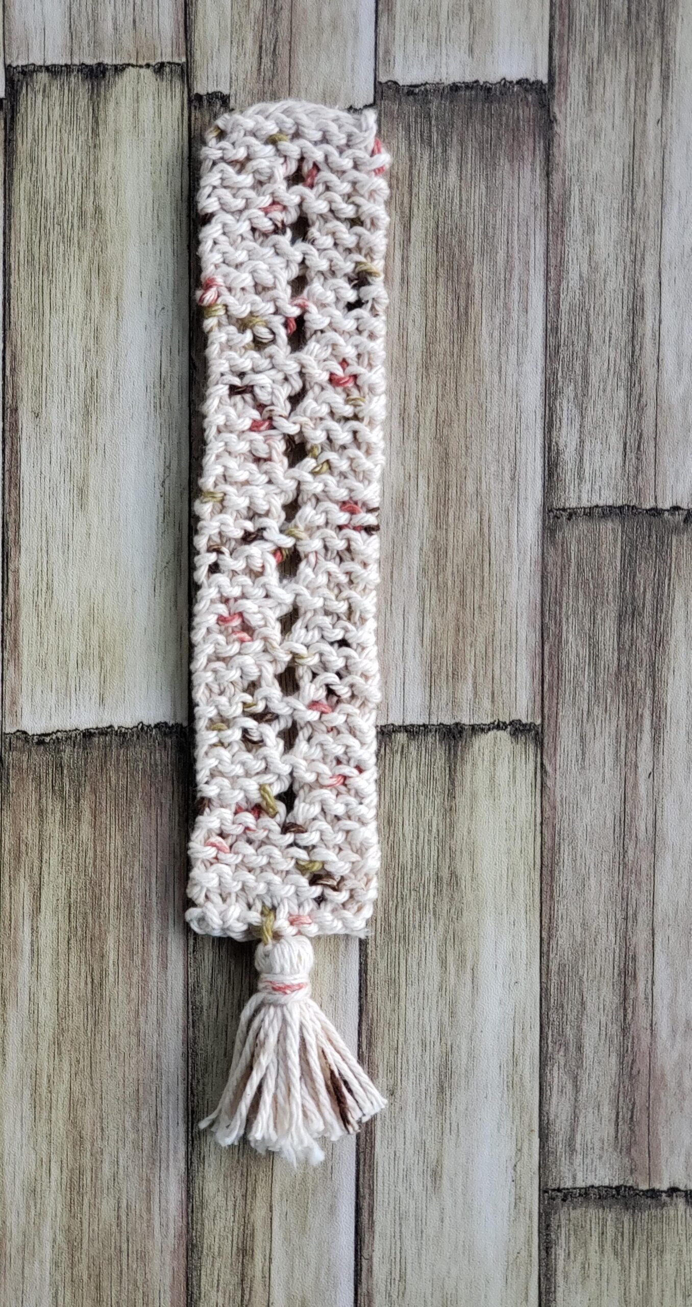 Speckled Knit Bookmark Pattern for Beginners Flat lay of completed speckled knitted bookmark with mini tassel on rustic wood background.