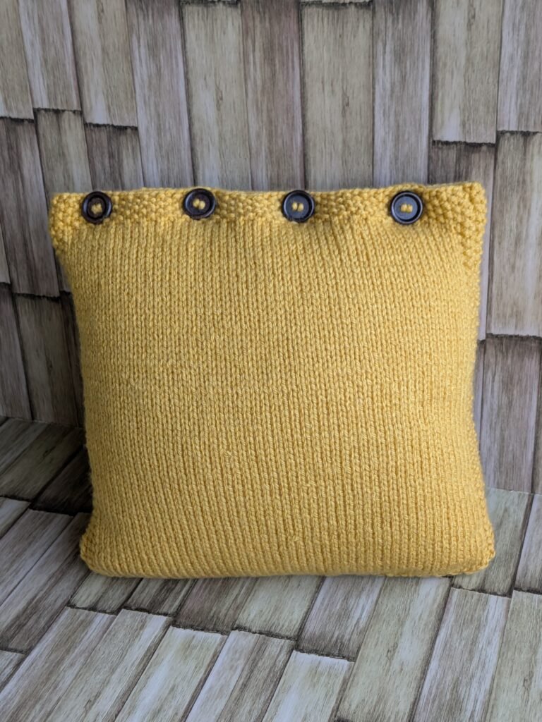 The Goldenrod Leaf Pillow: Free Knit Pillow Cover Pattern Back closure of the hand-knit pillow cover showing four dark round wooden buttons fastened along the top seed-stitch band.