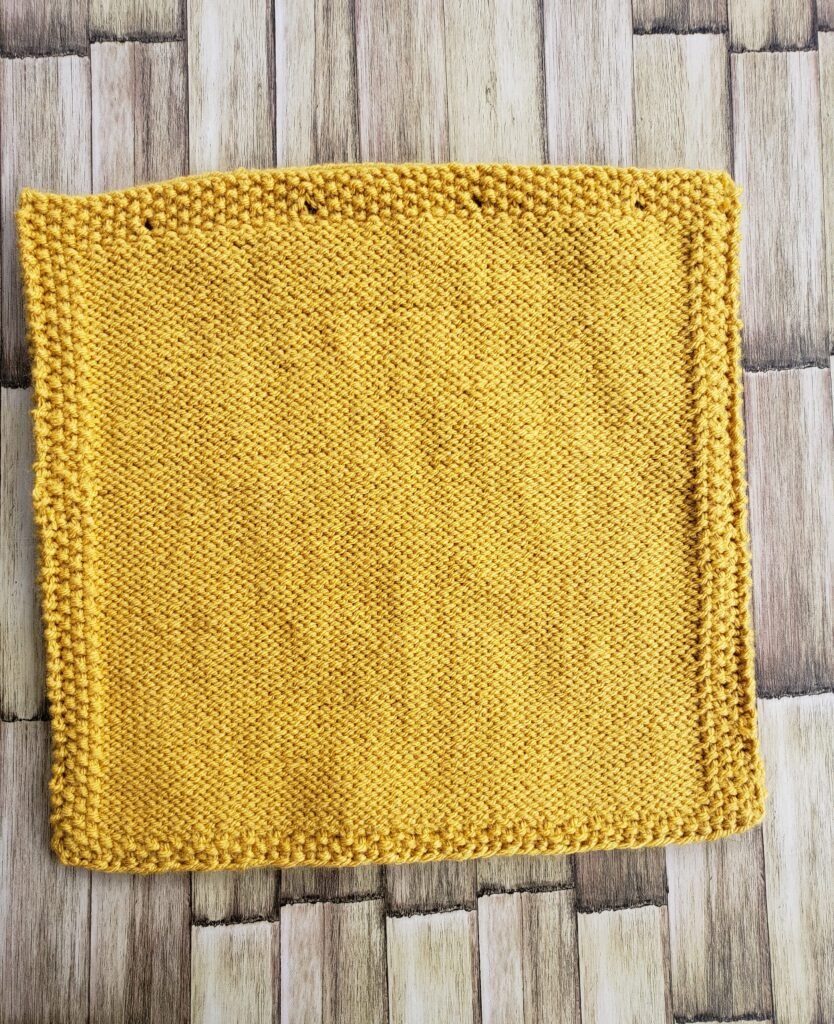 The Goldenrod Leaf Pillow: Free Knit Pillow Cover Pattern Steam-blocked square knitted back panel with seed stitch borders and integrated top buttonholes lying flat before assembly.