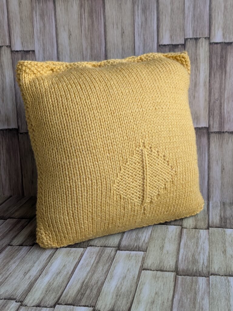 The Goldenrod Leaf Pillow: Free Knit Pillow Cover Pattern Side angled view of a chunky mustard yellow knitted cushion cover showing clean seed stitch borders and plush pillow depth.